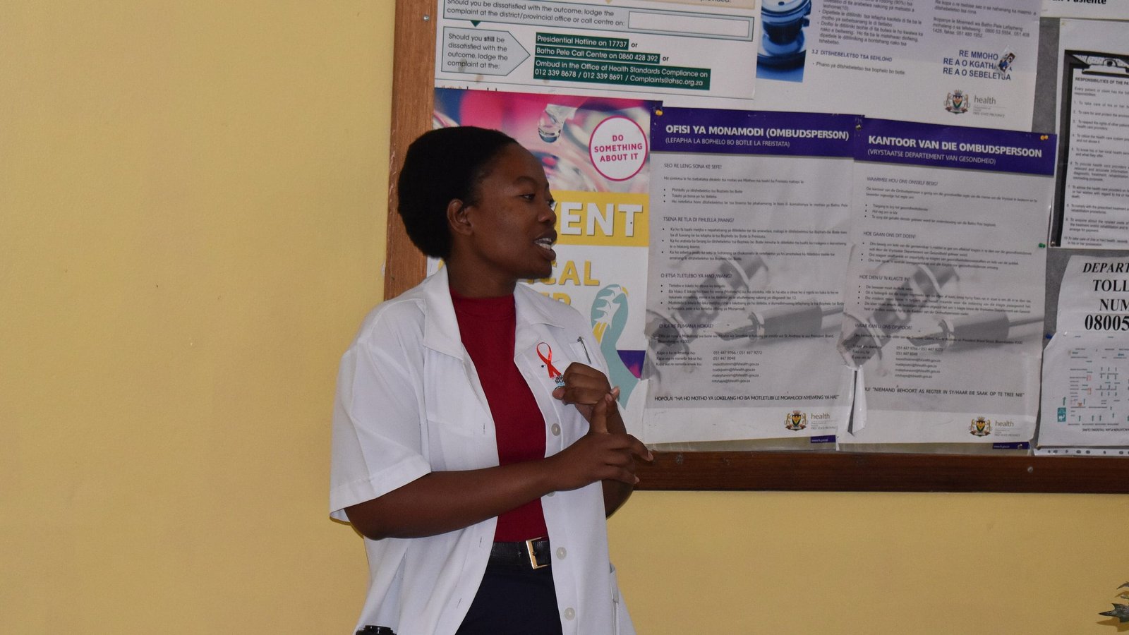 A community health worker presenting to patients beside clinic health notices