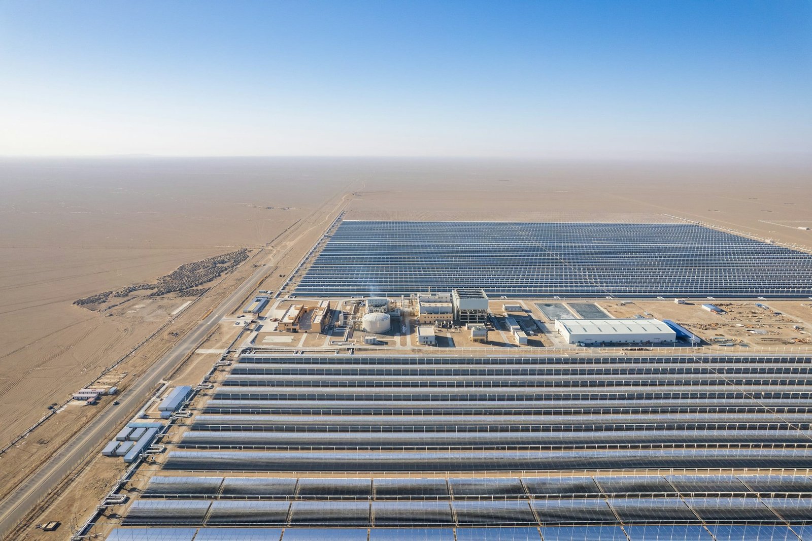Aerial view of a large solar array laid out in long parallel rows across open desert